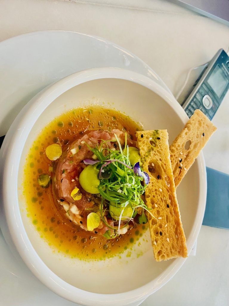 A clear broth poured over shellfish, with a seeded crisp
