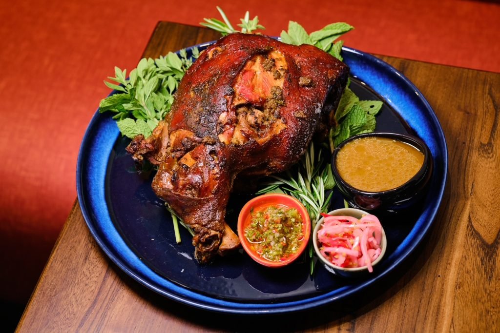 A whole roast pork shoulder with salsas and pickled onion