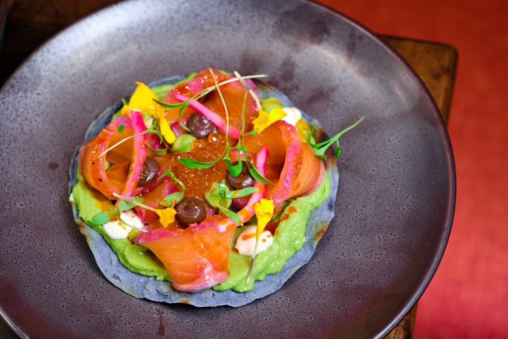 A tostada with avocado, cured fish and pickled onion