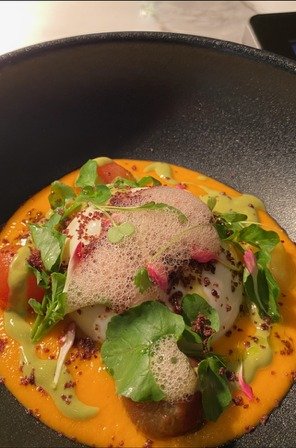 A course in a dark bowl under a citrus foam